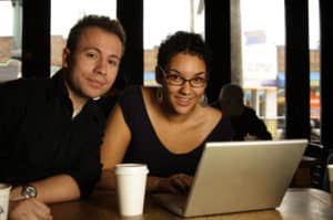 a man and women at a counter next to a computer laptop with a drink cup collaborating