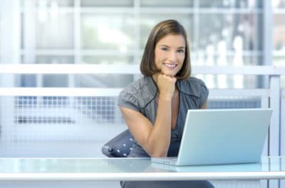 Woman at her desk smiling at the camera with a laptop