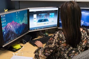 woman using three monitors on her computer desk in an office with the internet