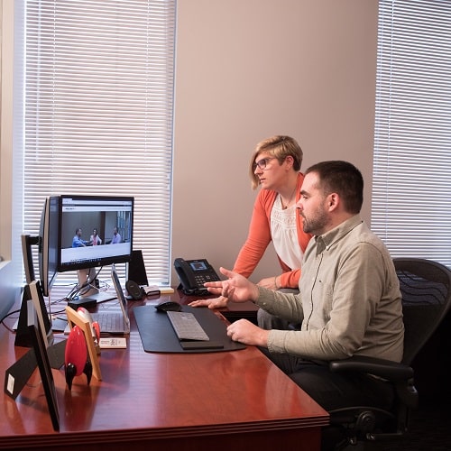 two team members at a desk talking about what is on computer