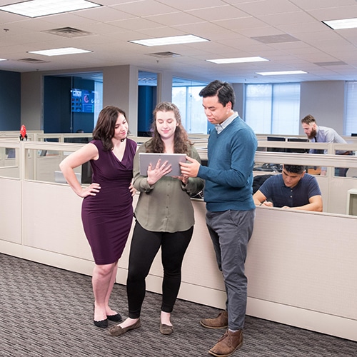 three team members in an office looking at a computer tablet